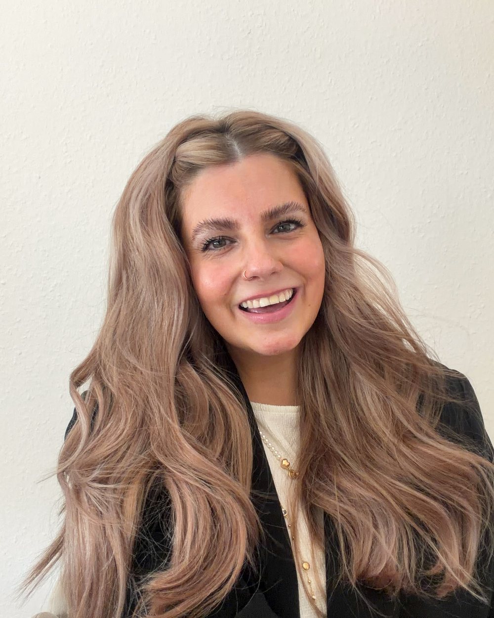 Selina Stefan, lächelnd, im schwarzen Blazer vor heller Wand